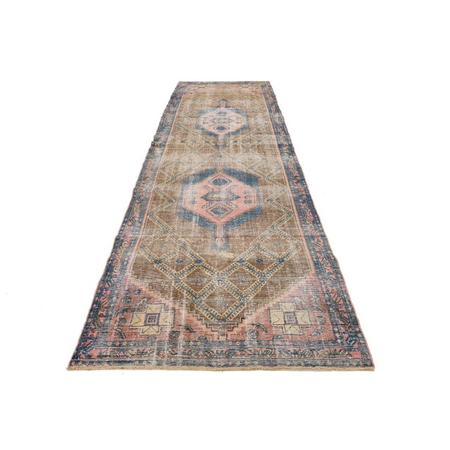 This vintage wool runner features a brown field with peach and blue tribal accents of Persian origin. This rug measures...