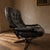A vintage Scandinavian-style lounge chair from the 1970s, featuring black tufted leather upholstery and an elegant...
