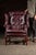 High-back wing chair and matching ottoman upholstered in deep oxblood red leather with brass nailhead trim and mahogany-...