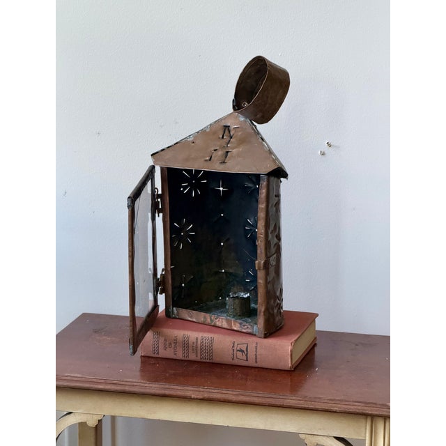 A charming antique handcrafted punched tin and copper lantern featuring hand-cut starburst motifs, a hinged glass door,...