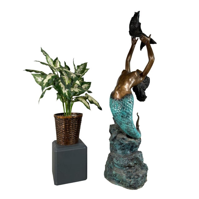 Large-scale bronze fountain sculpture depicting a graceful mermaid rising from a rocky outcrop and holding a fish above...