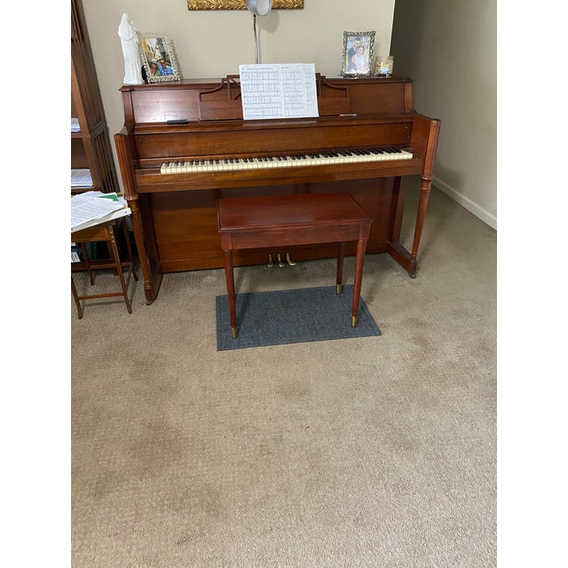 Mahogany-finished wood piano bench has a rectangular top with a hinged lid for sheet music storage. The piece is...