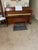 Mahogany-finished wood piano bench has a rectangular top with a hinged lid for sheet music storage. The piece is...