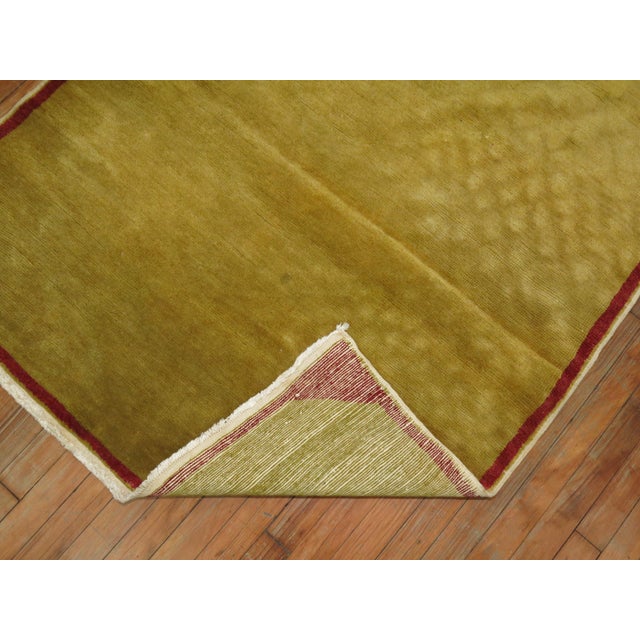 A vintage Turkish rug with a pea green field outlined with a thin red narrow border.