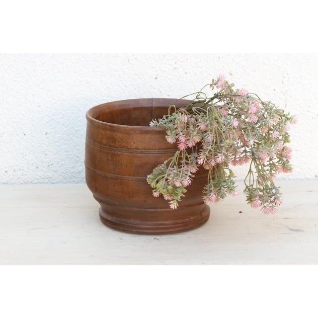 A broad, rounded-belly bowl turned from warm honey-brown wood, finished at the base with a stepped, flared foot that lifts...