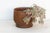 A broad, rounded-belly bowl turned from warm honey-brown wood, finished at the base with a stepped, flared foot that lifts...