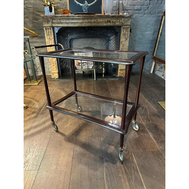 An Italian bar cart or drinks trolly circa 1950. In brass and walnut with two shaped tiers banded in brass, tooled handle...