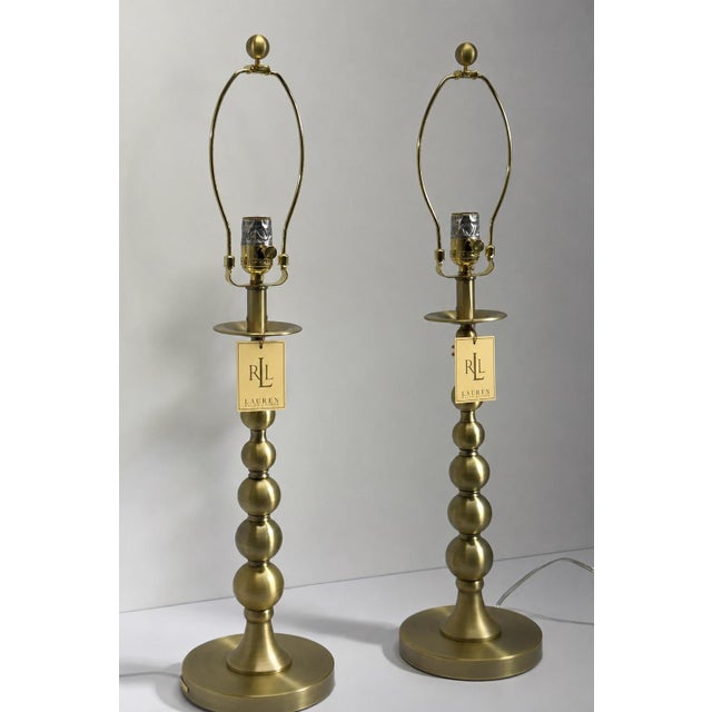A refined pair of Ralph Lauren buffet lamps featuring a warm antique brass finish and elegantly turned ball-form stems....
