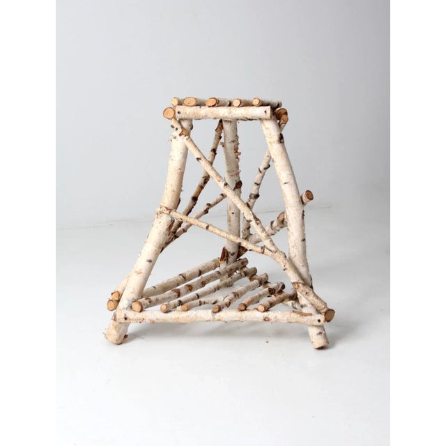 This is a vintage birch bark table, a rustic folk art end table with a three-leg base, a slatted lower shelf, and a...