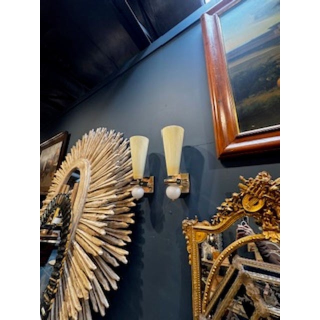 The product is a pair of modern ivory and white colored Murano cone shape sconces on brass bases. These sconces are likely...