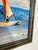 This vintage oil painting captures a serene maritime scene, depicting a sailboat gliding across calm blue waters under a...