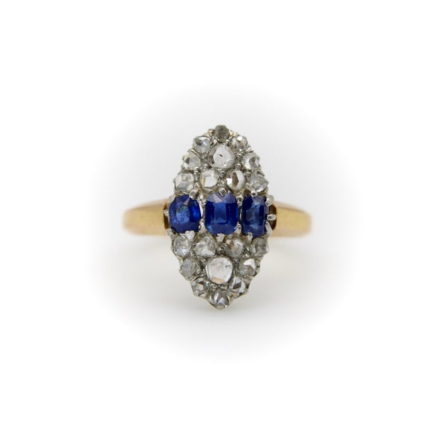 This is a classic navette shaped ring with a band of three rectangular faceted natural blue sapphires. The face of the...