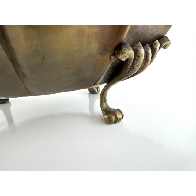 A vintage hammered brass bowl featuring a beautifully scalloped rim, ornate foliate side handles, and four sculptural claw...