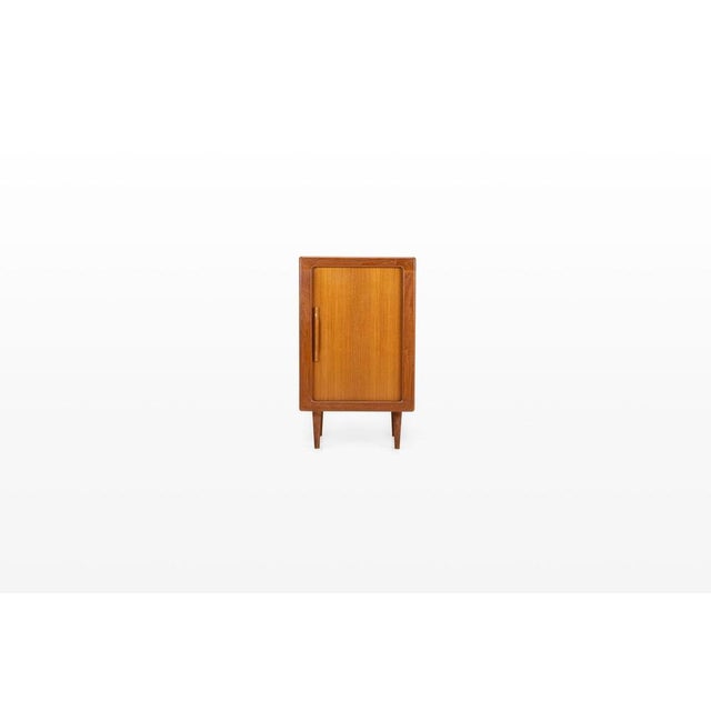 Charming Danish vintage cabinet in teak featuring a sleek tambour door and two wooden shelves. with its compact design and...