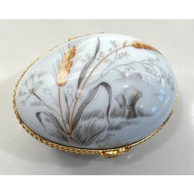 This charming artist signed Limoges box has been made in the form of an egg and sports a hand painted gold ear of rye...