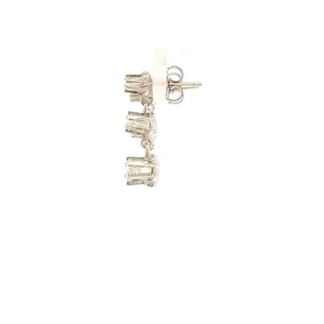 A pair of drop earrings featuring round-cut diamonds. Crafted in 14k white gold, each earring showcases three white...