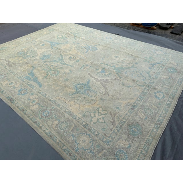 This handmade wool rug embodies the soft elegance of Oushak design with its faded ivory and blue palette and graceful...