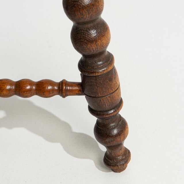 A 20th century stool crafted in oak, featuring a traditional bobbin-turned leg structure. The design emphasizes...