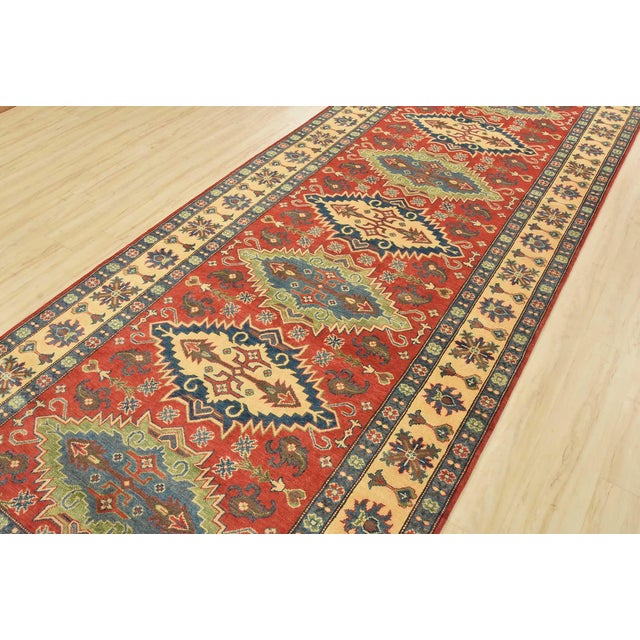 A traditional tribal Caucasian Kazak runner hand-knotted with an all-wool pile on a cotton foundation. This oriental rug...