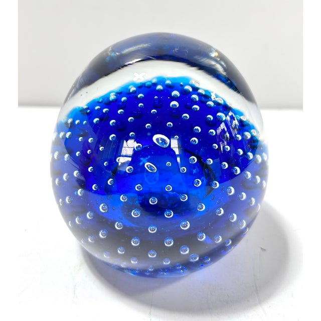 Striking Murano-style cobalt blue art glass paperweight featuring a rich blue core encased in clear crystal with suspended...