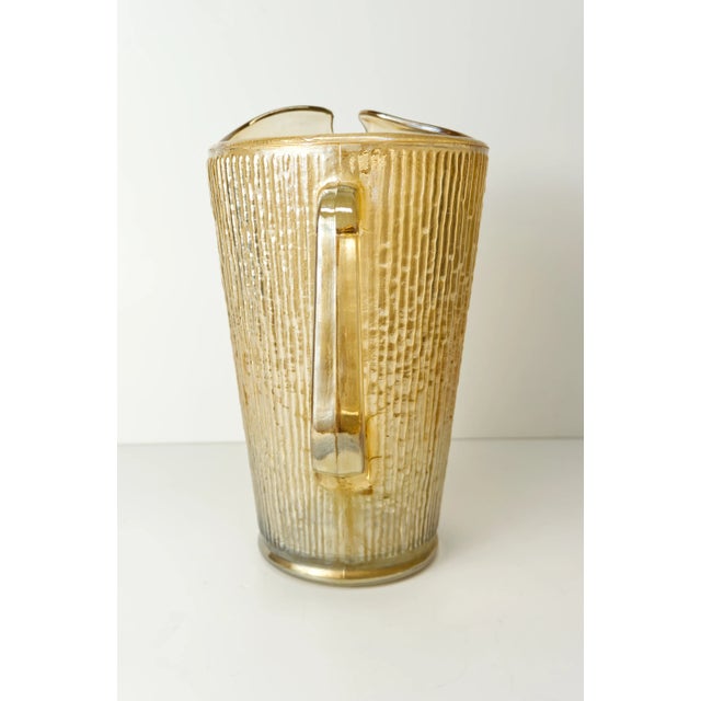An iridescent carnival glass ribbed bark textured pitcher in a marigold orange color attributed to the Jeanette Glass...
