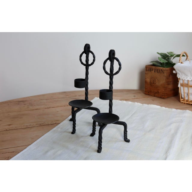 Black metal candlesticks, crafted in a brutalist style with twisted iron supports, decorative rings, and a graphic...