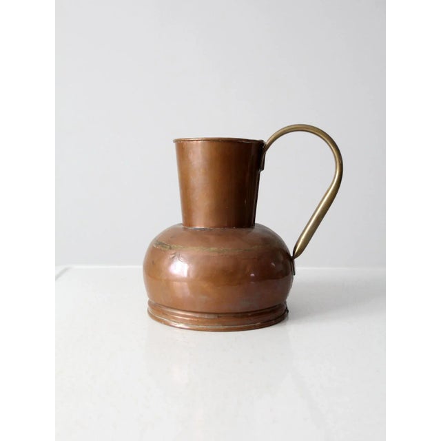This antique Dutch copper ewer features a well-crafted, sculptural form with a prominent curving brass handle and a...