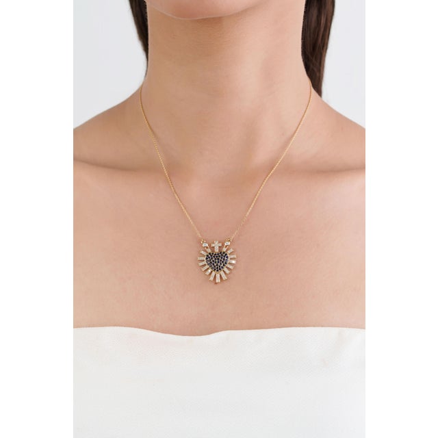 This modern Sacred Heart pendant necklace showcases a vibrant 1ct blue sapphire, set in 14K yellow gold. The sapphires...
