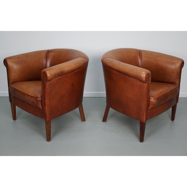 This pair of cognac-colored leather club chairs come from the Netherlands. They are upholstered with patinated cognac-...