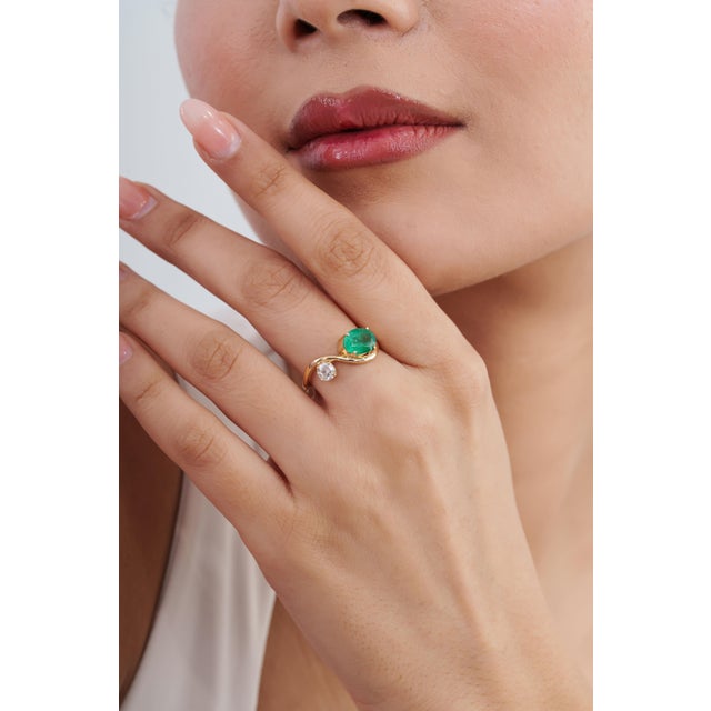This elegant Toi et Moi bypass ring features a 1.41-carat oval-cut natural green emerald, set in 14k yellow gold. The...