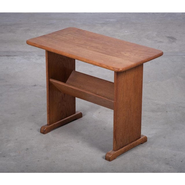 Charming side table with integrated magazine holder, crafted in solid oak and produced in Denmark during the 1960s. A...