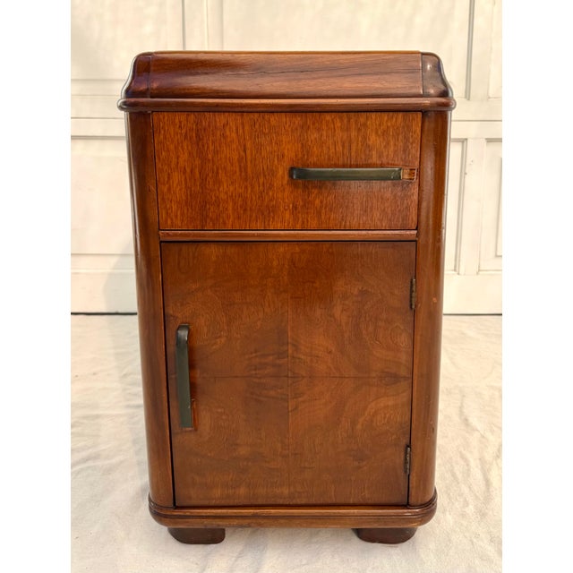 This finely crafted vintage Art Deco nightstand from the 1930s–1940s features sculptural rounded edges, warm wood grain,...