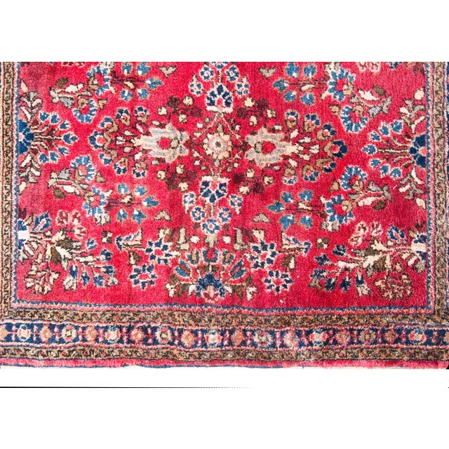 A petite early 20th century Persian Sarouk rug with a mirrored floral pattern across the field, surrounded by a simple...