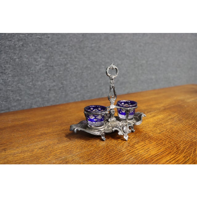 Ornate antique double open salt cellar featuring two cobalt blue glass liners set within an elaborate silver-tone metal...