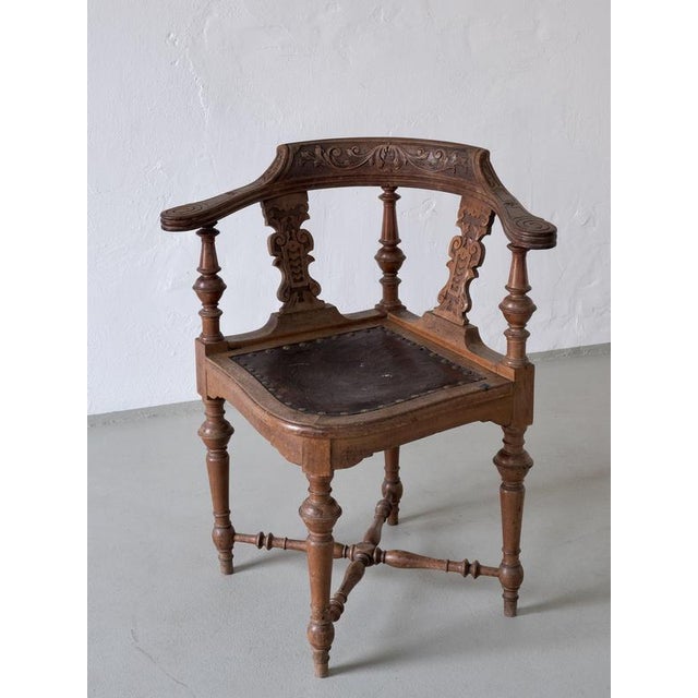 Ornate corner chair featuring a curved, carved backrest and turned wood frame. The seat is upholstered in embossed leather...