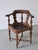 Ornate corner chair featuring a curved, carved backrest and turned wood frame. The seat is upholstered in embossed leather...