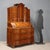 Walnut, maple burl, and various wood trim trumeau. Upper section with a tripartite leaf-spring drawer, surmounted by a...