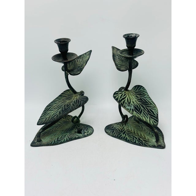 Brief description: Pair of vintage metal candlesticks featuring a nature-inspired design with lily pads, curved stems, and...
