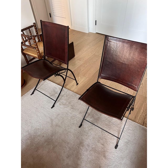 A matched set of four antique French folding chairs, late 19th century. Each chair pairs a blackened wrought iron folding...