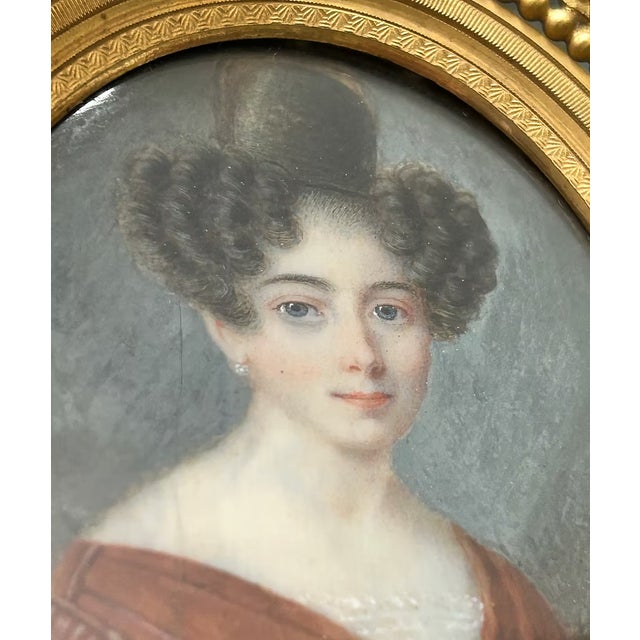 An elegant early 19th century portrait miniature depicting a young woman with softly curled coiffure and a rich russet...