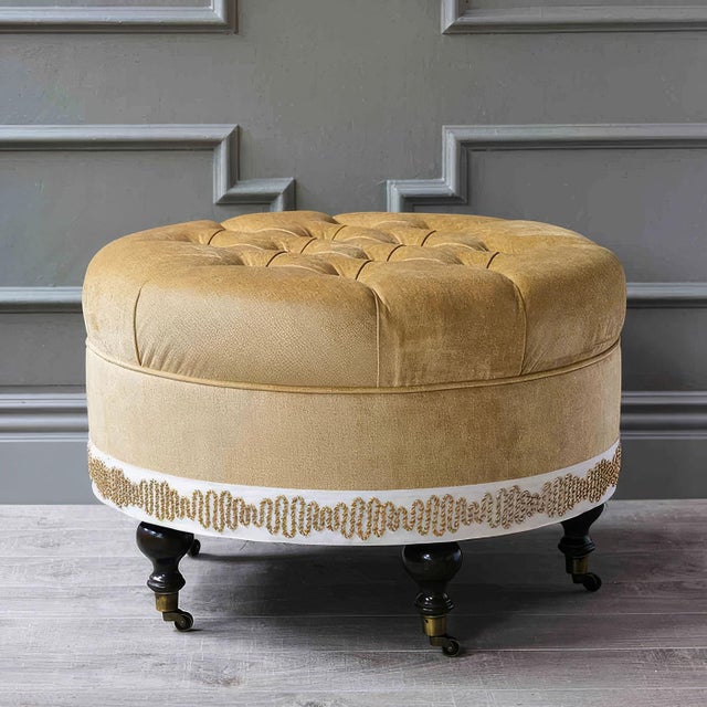 Upholstered in sumptuous gold velvet fabric, this glamorous ottoman features exquisite button tufting and decorative trim...
