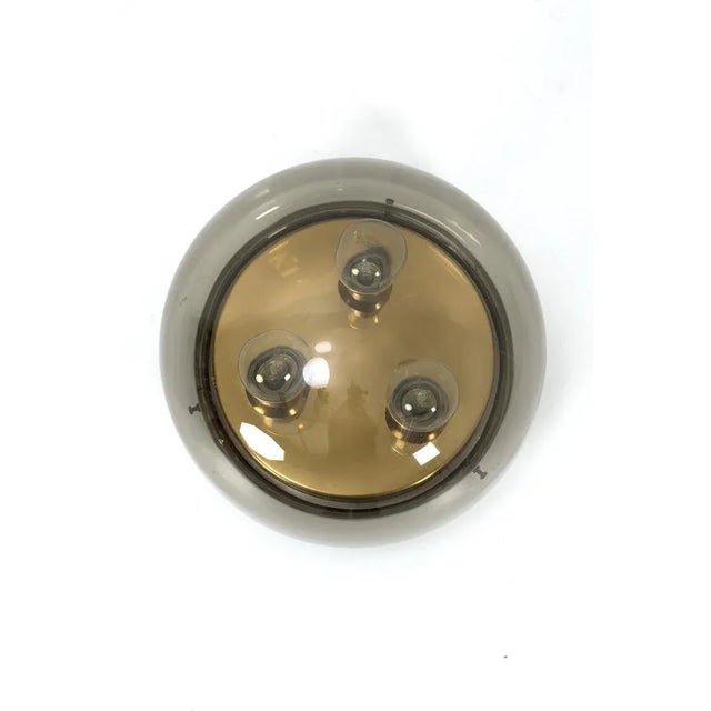 Smoked glass and brass ceiling lamp with 3 light sources. In good vintage condition. Measurements D. 19 cm; Ø 30 cm. Up to...
