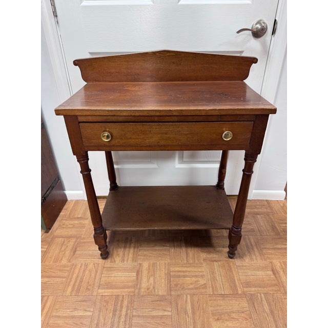 A mid-19th century American washstand in cherry, in the late Sheraton taste. A gabled splashboard with scrolled ends rises...