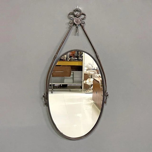 Oval brass wall mirror. The load-bearing structure is composed of two decorated round-section arms joined at the top by a...