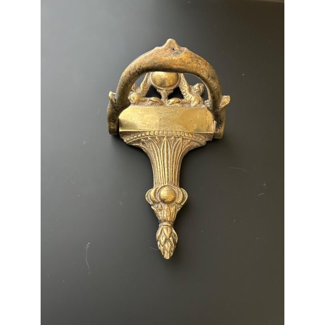 An impressive vintage solid brass door knocker with an ornate Neoclassical-inspired design. The substantial cast brass...
