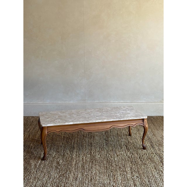 This vintage coffee table features a marble top with warm creams, eggshell beiges, and soft taupe movement over a carved...