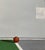 This artwork depicts a minimalist basketball court scene, focusing on a lone hoop and a solitary basketball resting on the...