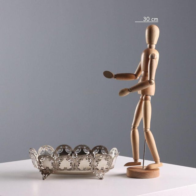 A basket in embossed, chased, and pierced silver, supported by feet with leaf-shaped scrolls. Silver stampings are...