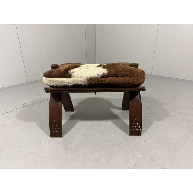 Camel saddle stool. Cowhide covered seat fastened with leather laces on a wooden frame with metal details. 1960-70’s. In...