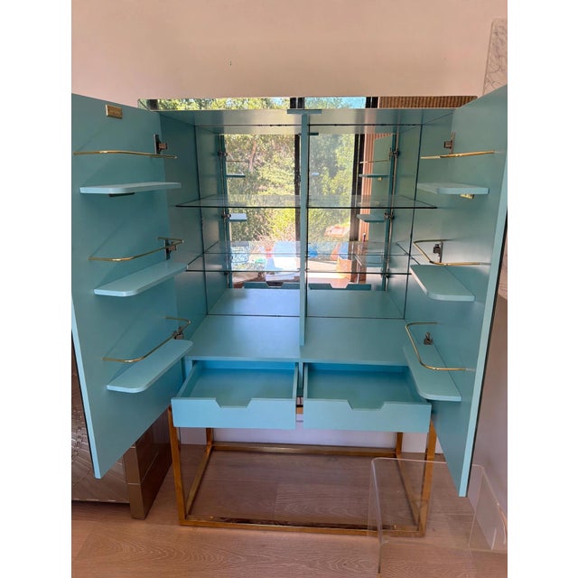 Jonathan Adler Delphine Bar in brass and mirror. Antiqued mirrored exterior with polished brass base; double doors open to...